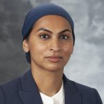 headshot of Dr. Mehreen Kisat wearing a white shirt, dark suit jacket, and a blue head coveringing