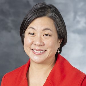 A grey photography background with a formal photo of Sandra Lin, MD, smiling with black hair and a red jacket.