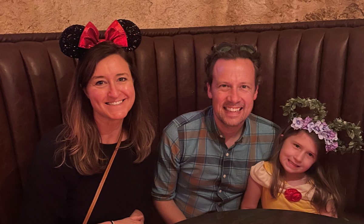 Dr. Hanson wears Minnie Mouse ears with her husband Nick and daughter Rori at a booth in a restaurant in Disneyland.