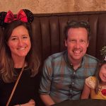 Dr. Hanson wears Minnie Mouse ears with her husband Nick and daughter Rori at a booth in a restaurant in Disneyland.