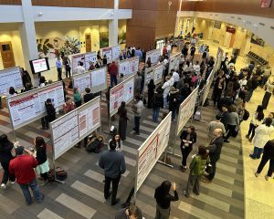 Many people gather around several posters in an atrium