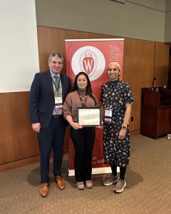 Drs. Patrick Varley, M. Kristine Carbullido, and Mehreen Kisat stand in front of a banner that says "Wisconsin Surgery." Dr. Carbullido holds an award certificate.