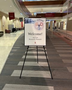 A poster sits on an easel in an atrium with the words "Welcome! to the Annual Research Summit"
