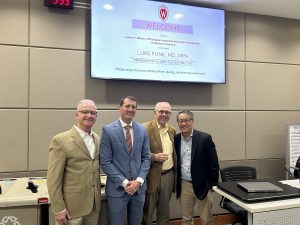 Drs. Michael Bentz, Luke Funk, Layton Rikkers, and Herb Chen stand together under a tv screen that is welcoming people to the investiture ceremony