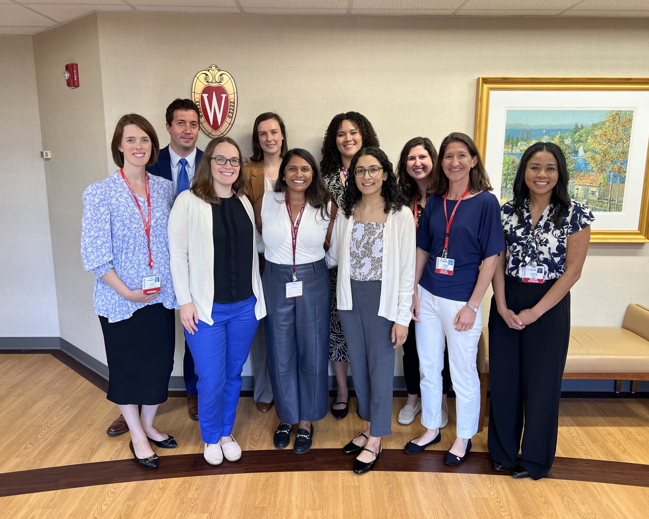 A group of ten fellows stand together for a picture indoors with the UW Crest behind them